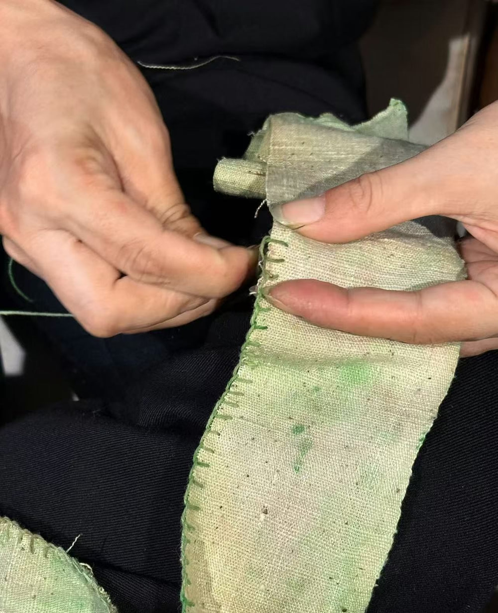 Hands holding a pale green cloth with visible hand stitching along its edge.