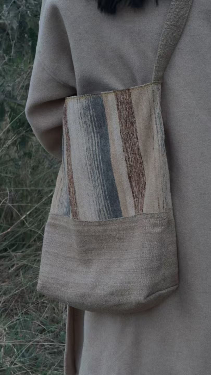 A person in a beige coat carrying a grey-beige shoulder bag with a vertically striped panel.