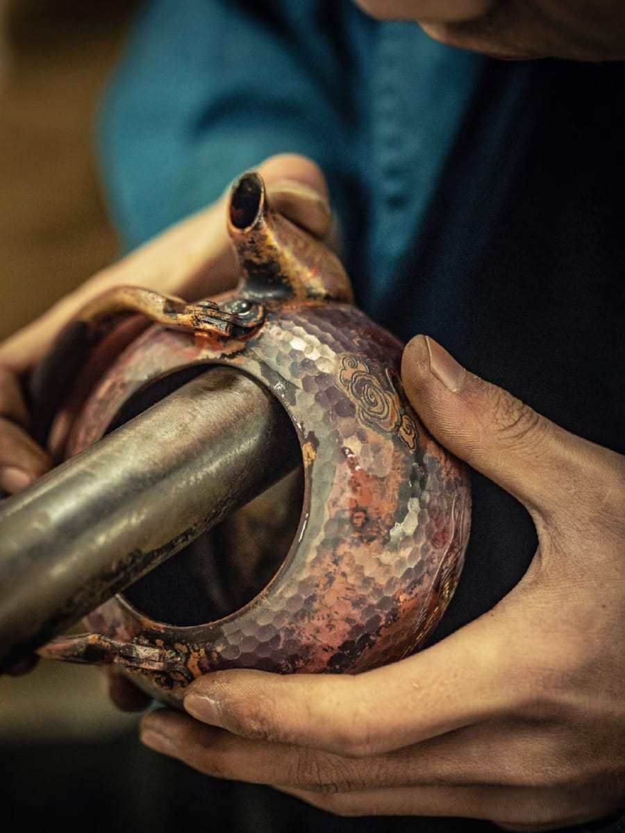 A maker's hands shaping a hammered copper vessel