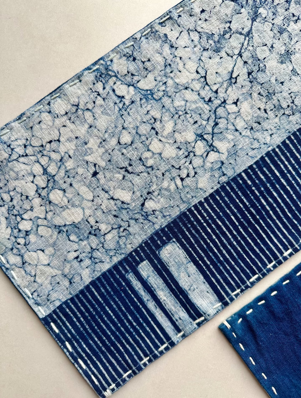 Indigo-dyed cloth with a white crackle pattern above blue and white stripes, with white hand stitching along the seam.